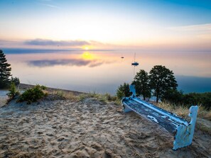 A bench on a sandy beach with a calm body of water and a clear sky in the background. - 4 Star Holiday Home in Borkop (Borkop)