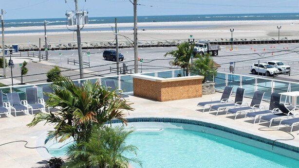 A pool area with lounge chairs and a palm tree, overlooking a beach. - Steps Away From All the Fun (Wildwood)