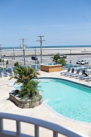 A pool area with lounge chairs and a palm tree, overlooking a beach.