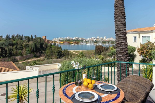 A balcony with a table set for two, overlooking a marina and cityscape.