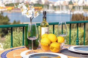 A table with a wine bottle, glasses, and a bowl of lemons, set against a scenic waterfront view.