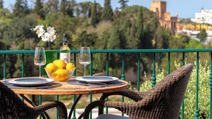 A table set with plates, glasses, a bottle, and lemons on a balcony with a view of greenery and buildings. - Townhouse 12 with amazing sea views (Ferragudo)