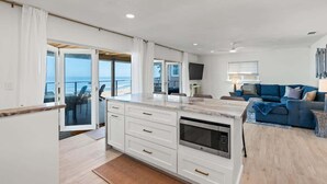 Una cocina moderna con una isla grande, armarios blancos y vista al océano.