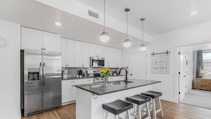 A modern kitchen with white cabinets, stainless steel appliances, a central island with bar stools, and pendant lighting.