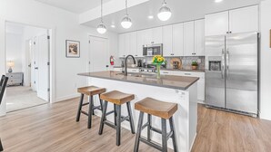 Une cuisine moderne avec des meubles blancs, des appareils en acier inoxydable et un îlot central doté de tabourets de bar.