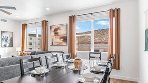 Un coin repas avec une table dressée pour quatre personnes, un canapé en arrière-plan et une fenêtre donnant sur un paysage désertique.
