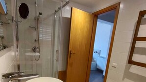 A modern bathroom with a large oval sink, a separate pedestal sink, a glass-enclosed shower, and a wooden door leading to another room. - Foresteria Mongerrati (Isnello)