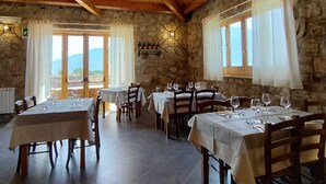 A rustic dining area with stone walls, wooden beams, and multiple tables set for dining. - Foresteria Mongerrati (Isnello)