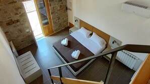 A bedroom with a wooden ceiling, a stone wall, a bed with white linens, and a radiator. - Foresteria Mongerrati (Isnello)