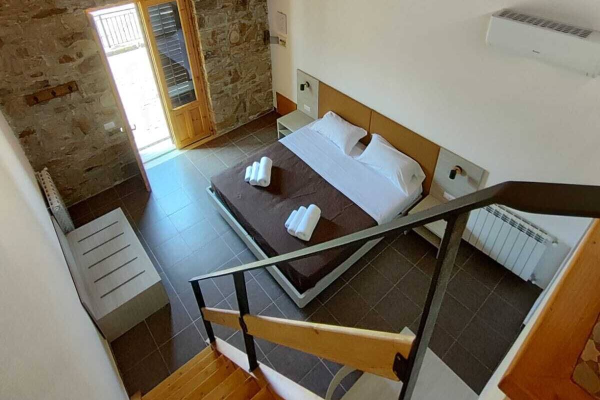 Quarto com teto de madeira, parede de pedra, cama com roupa de cama branca e radiador.
