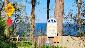 A beach sign with 'Road Ends' and 'No Lifeguard on Duty' warnings, a wooden fence, and a view of the ocean.