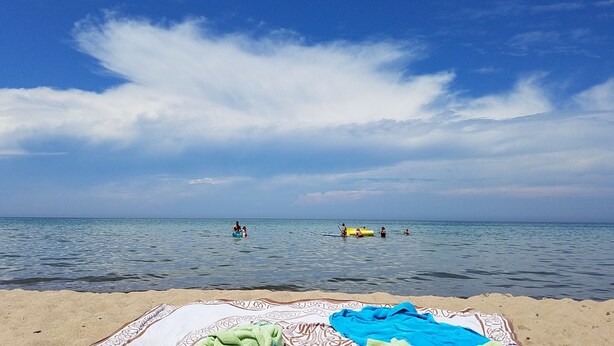 A beach with a blanket and towels on the sand, a calm sea, and a partly cloudy sky.