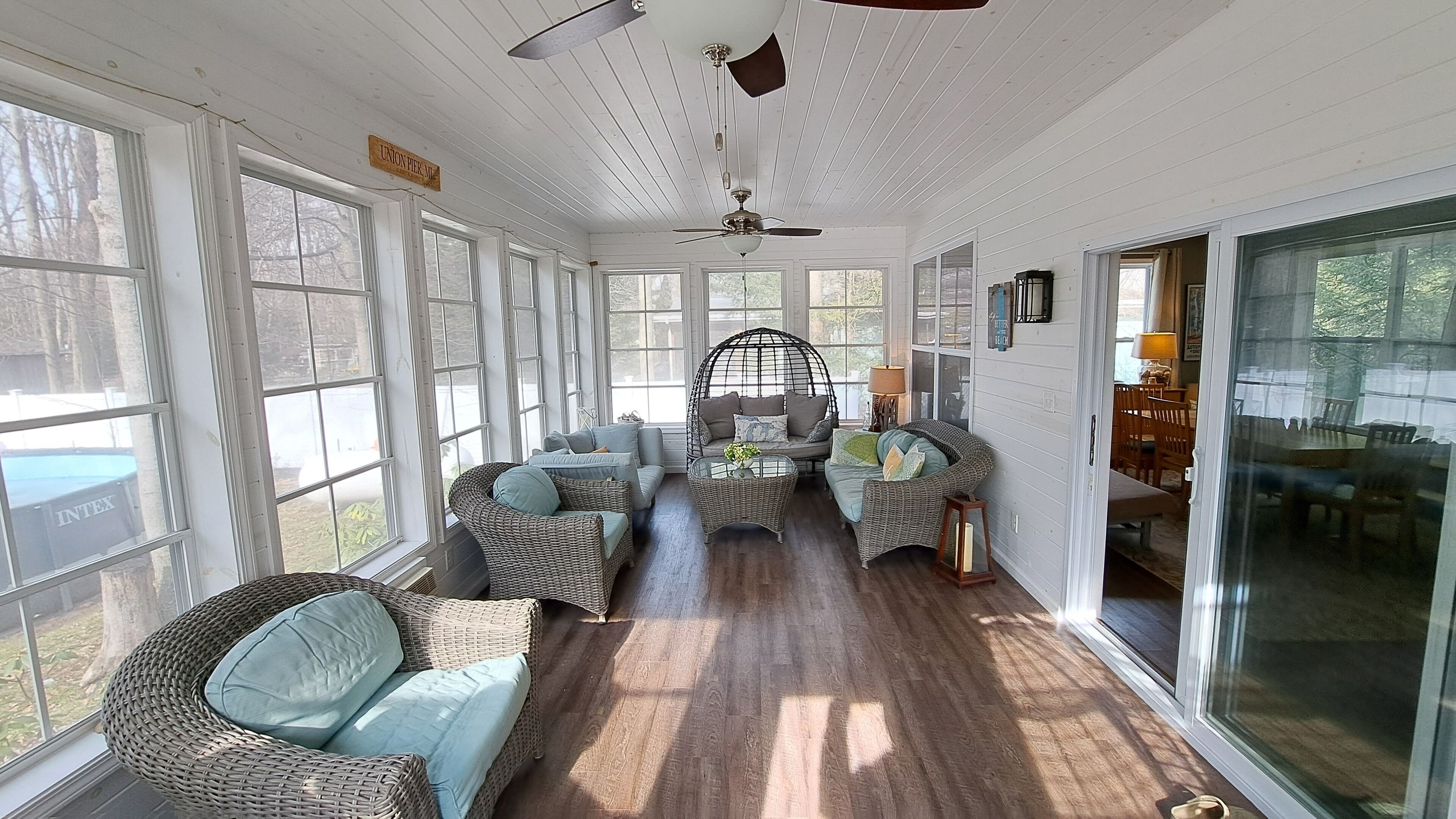 A sunroom with wicker furniture, large windows, and a ceiling fan.