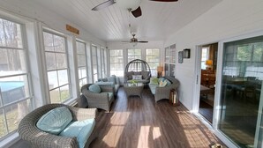 A sunroom with wicker furniture, large windows, and a ceiling fan.