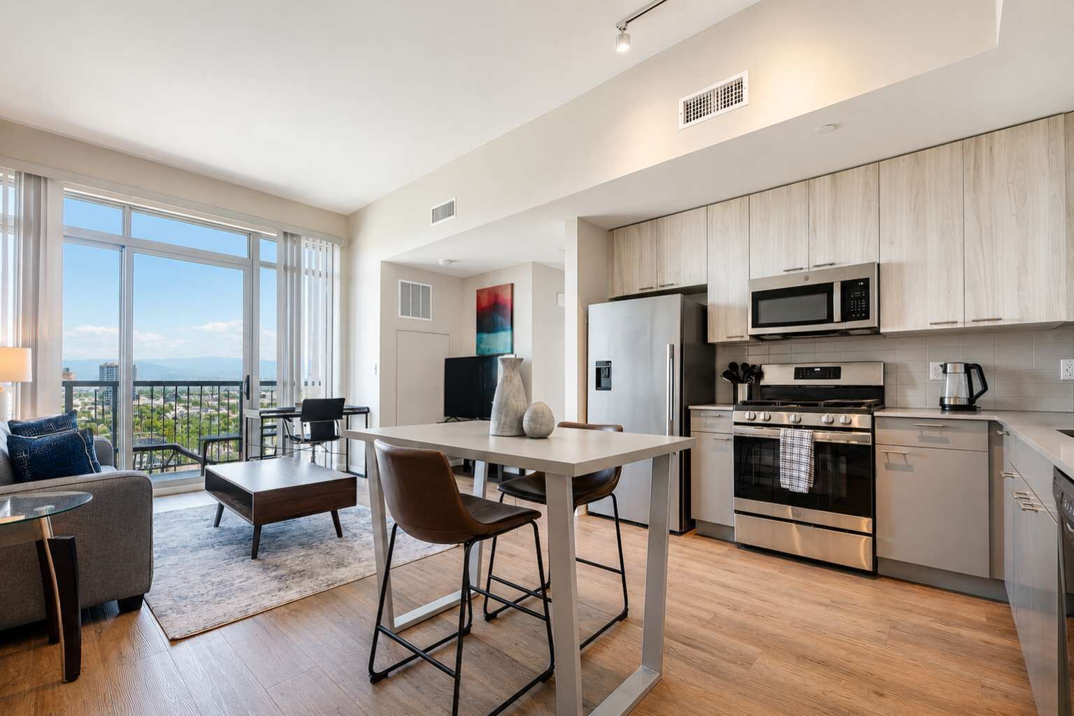 A modern kitchen with stainless steel appliances, a dining area with a table and chairs, and a balcony with a view.
