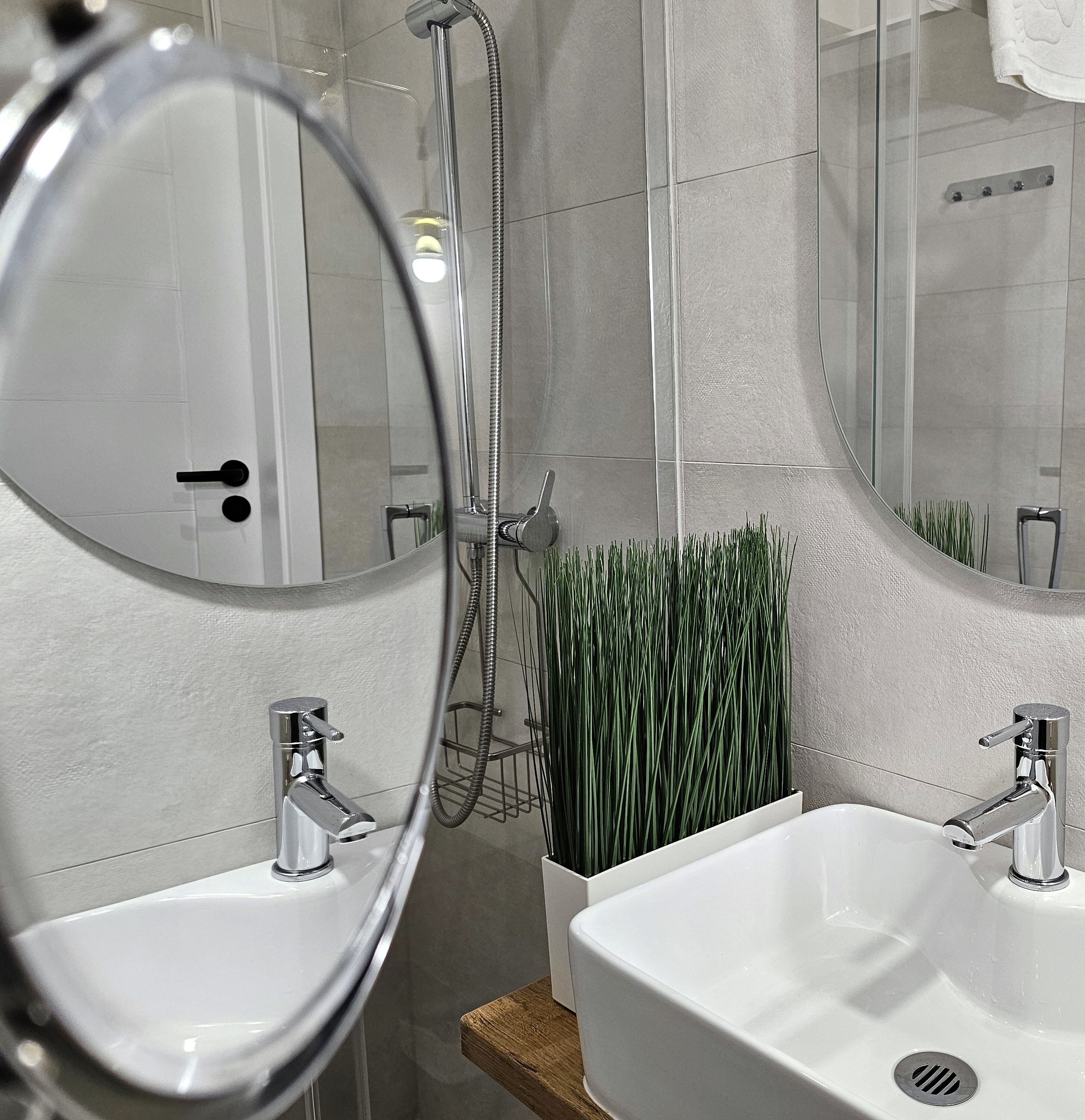 Een badkamer met twee wastafels, een douche en een spiegel.
