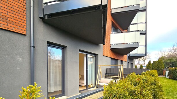 Eine moderne Wohnung mit Balkon, großen Fenstern und einem gepflegten Garten.