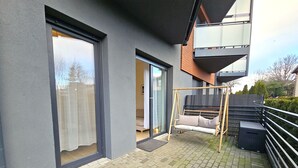 Eine moderne Wohnung mit einer Schiebetür, einem Balkon mit einer Couch und einer Schaukel, und Blick auf die Umgebung.