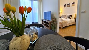 Ein modernes Wohnzimmer mit Essbereich, ausgestattet mit Fernseher, bequemen Sitzmöglichkeiten und einer Blumenvase.