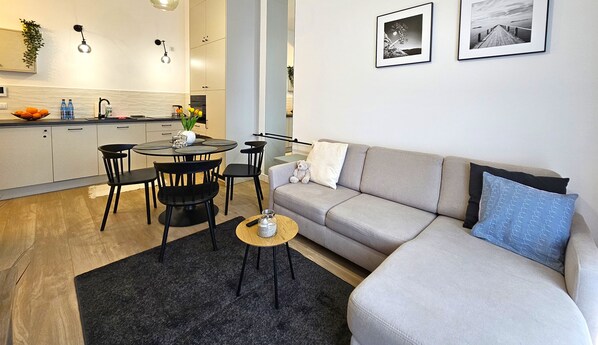 Una sala de estar moderna con un sofá gris, una mesa de centro y un comedor con una mesa redonda y sillas. Hay dos cuadros en la pared.