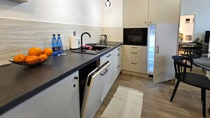 Eine moderne Küche mit schwarzem Arbeitsplatz, weißen Schränken und einem eingebauten Backofen. Es gibt eine Spüle, einen Wasserkocher und eine Schüssel Orangen auf der Arbeitsfläche.