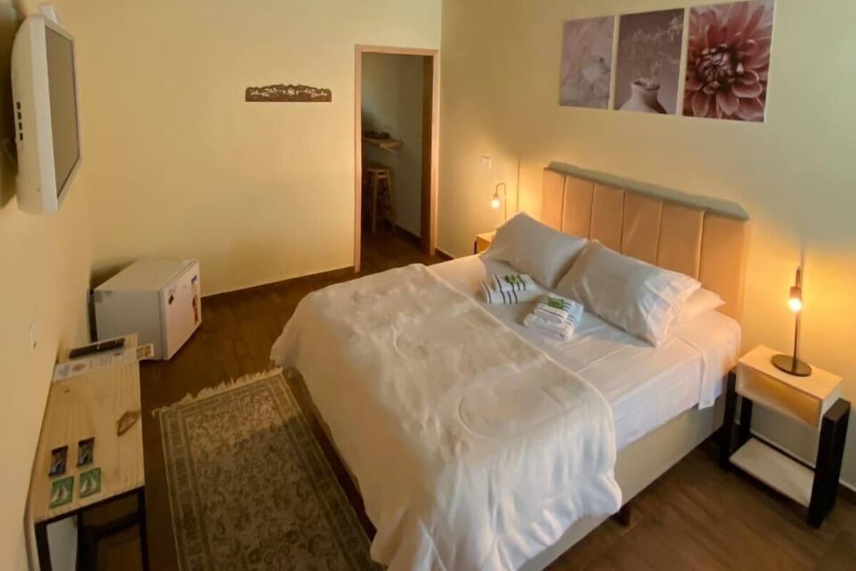 Ett sovrum med ett träpanelat tak, en säng med vita sängkläder, ett nattduksbord med en lampa och ett litet bord med en fjärrkontroll.