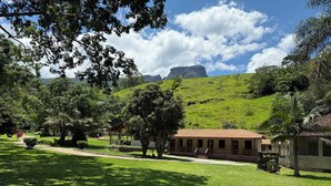 A lush green landscape with a building featuring a tiled roof and a small porch area. - Hospedaria Paiol (São Bento do Sapucaí)