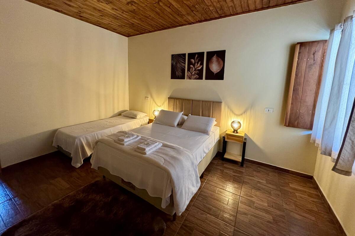 Ett rum med två sängar, trägolv, ett träpanelat tak och en väggmonterad lampa.