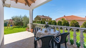 Eine überdachte Terrasse mit Tisch und Stühlen, einer Schaukel und Blick auf Häuser im Hintergrund.
