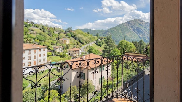 A balcony with wrought iron railings overlooking a hillside with buildings and a mountain in the distance. - Vacation Family Home in Tremezzo by Rent all Como (Tremezzina)