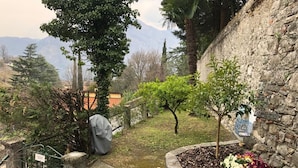 A garden with a stone wall, a small tree, and a flower bed. - Vacation Family Home in Tremezzo by Rent all Como (Tremezzina)