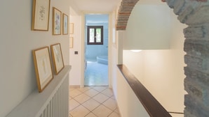 A hallway with framed pictures on the wall, a stone archway, and a view into another room. - Vacation Family Home in Tremezzo by Rent all Como (Tremezzina)