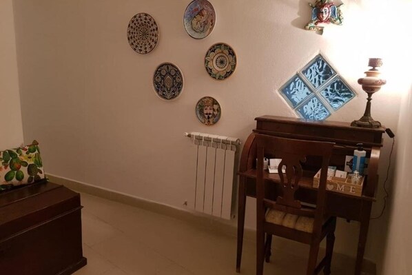 Une pièce avec un radiateur, une chaise en bois et une table sur laquelle se trouvent une lampe et des objets décoratifs.