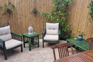 Un patio con mobiliario verde, incluyendo dos sillas y una mesa, y un pequeño farol.
