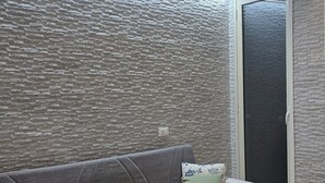 Ein modernes Wohnzimmer mit einer grauen Couch, einem schwarzen Teppich und einer strukturierten Wand.