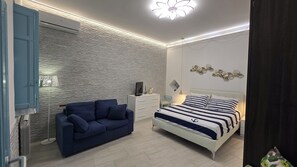 A bedroom with a bed, a blue sofa, a white dresser, and a wall-mounted air conditioner.
