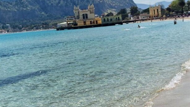 Eine Küstenlandschaft mit klarem türkisblauem Wasser, einem Sandstrand und einem historischen Gebäude mit Türmen.