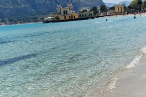 Un paysage côtier avec une eau turquoise et limpide, une plage de sable et un bâtiment historique doté de tours.