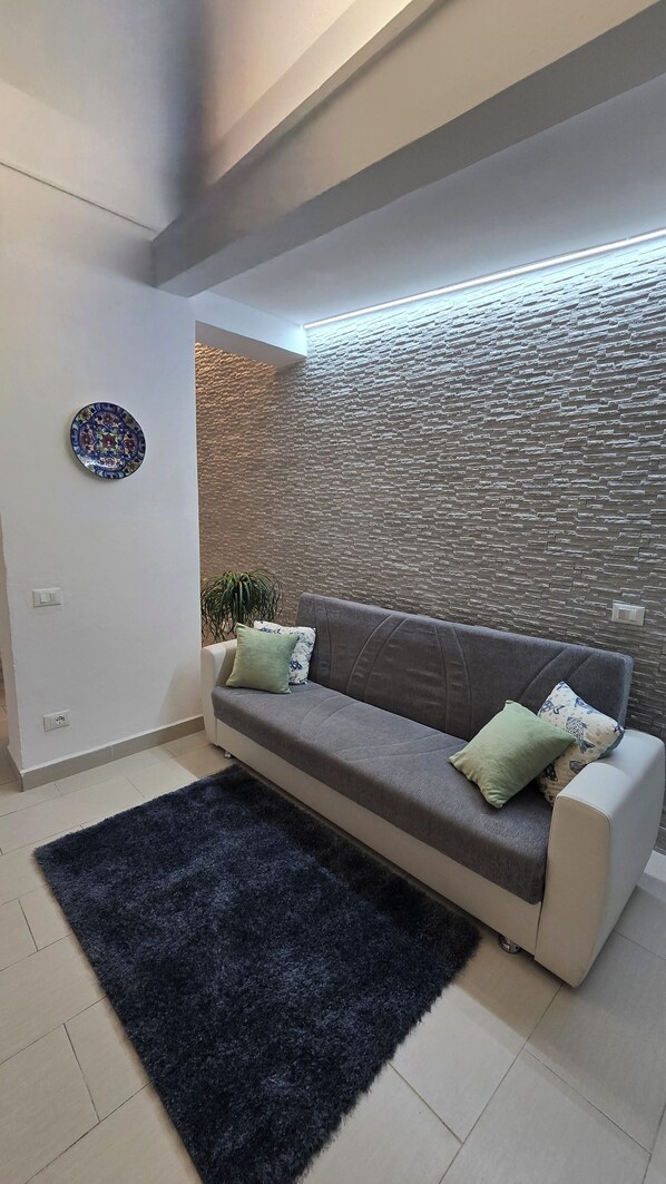 Una sala de estar moderna con un sofá gris, una alfombra oscura, un plato decorativo y una pared con textura.