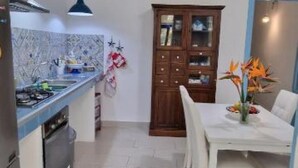 Eine Küche mit Herd, Spüle und Schränken. Ein Esstisch mit Stühlen und eine Blumenvase sind ebenfalls vorhanden.
