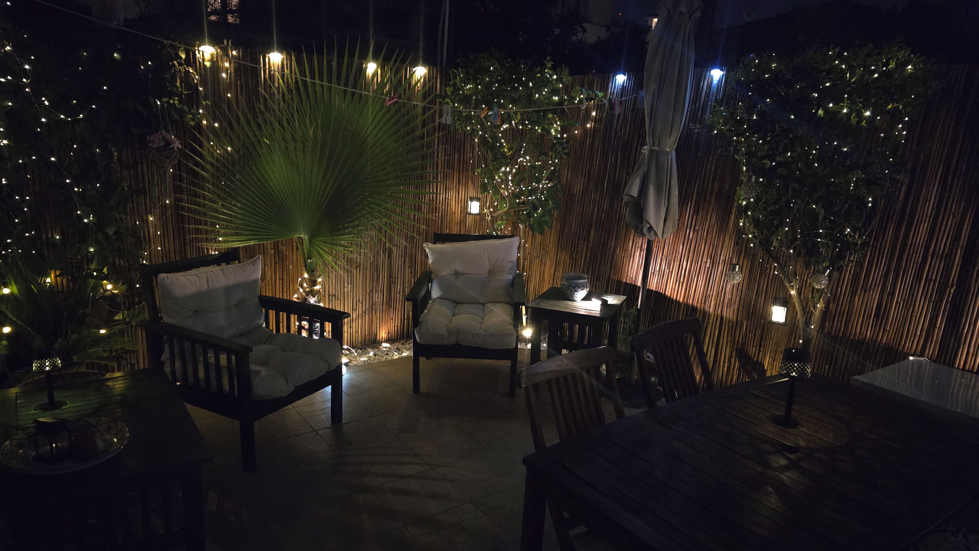 An outdoor seating area with chairs and tables, bamboo walls, and string lights.