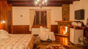 A cozy room with a bed, a fireplace, a television, and a stone wall. - Pousada Pau Brasil (Maringá)