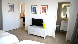 A hotel room with a bed, a TV on a white cabinet, a bathroom with a mirror, and three Paris-themed posters on the wall. - Studio Paris (Ivry-sur-Seine)