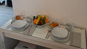 A dining area with a table set for two, including plates, cutlery, a bowl of fruit, and a croissant. - Studio Paris (Ivry-sur-Seine)