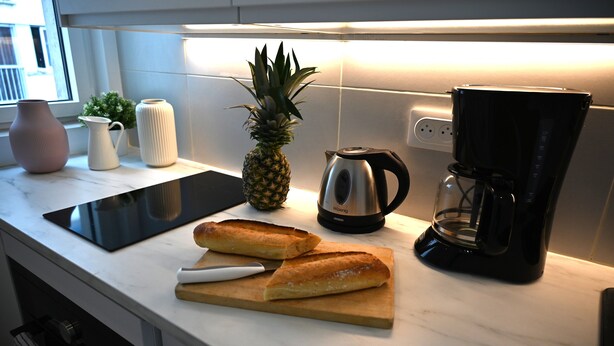 A kitchen counter with a pineapple, a coffee maker, and a cutting board with bread. - Studio Paris (Ivry-sur-Seine)
