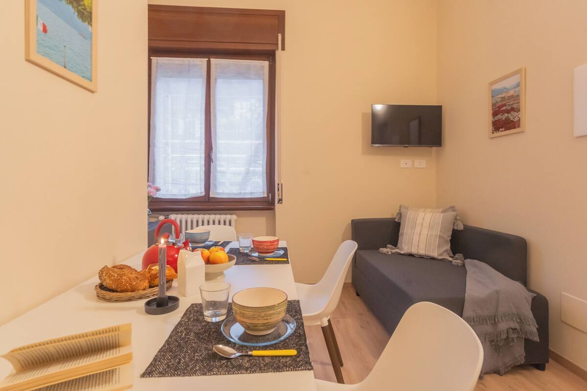 Een compacte leefruimte met een eethoek, een bank, een flatscreen-tv en een raam met zonwering.