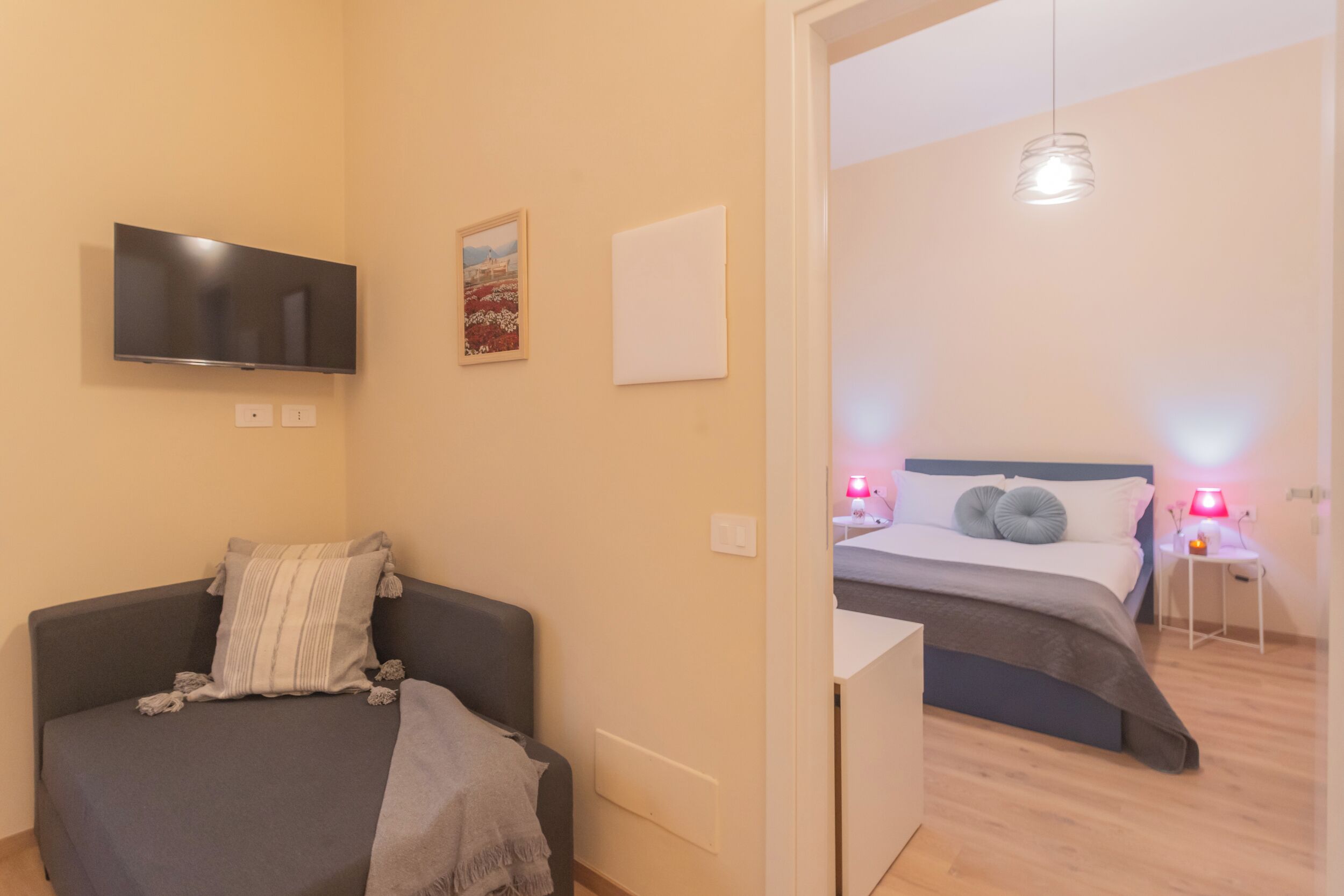 Quarto moderno com cama, mesas de cabeceira e televisão na parede.