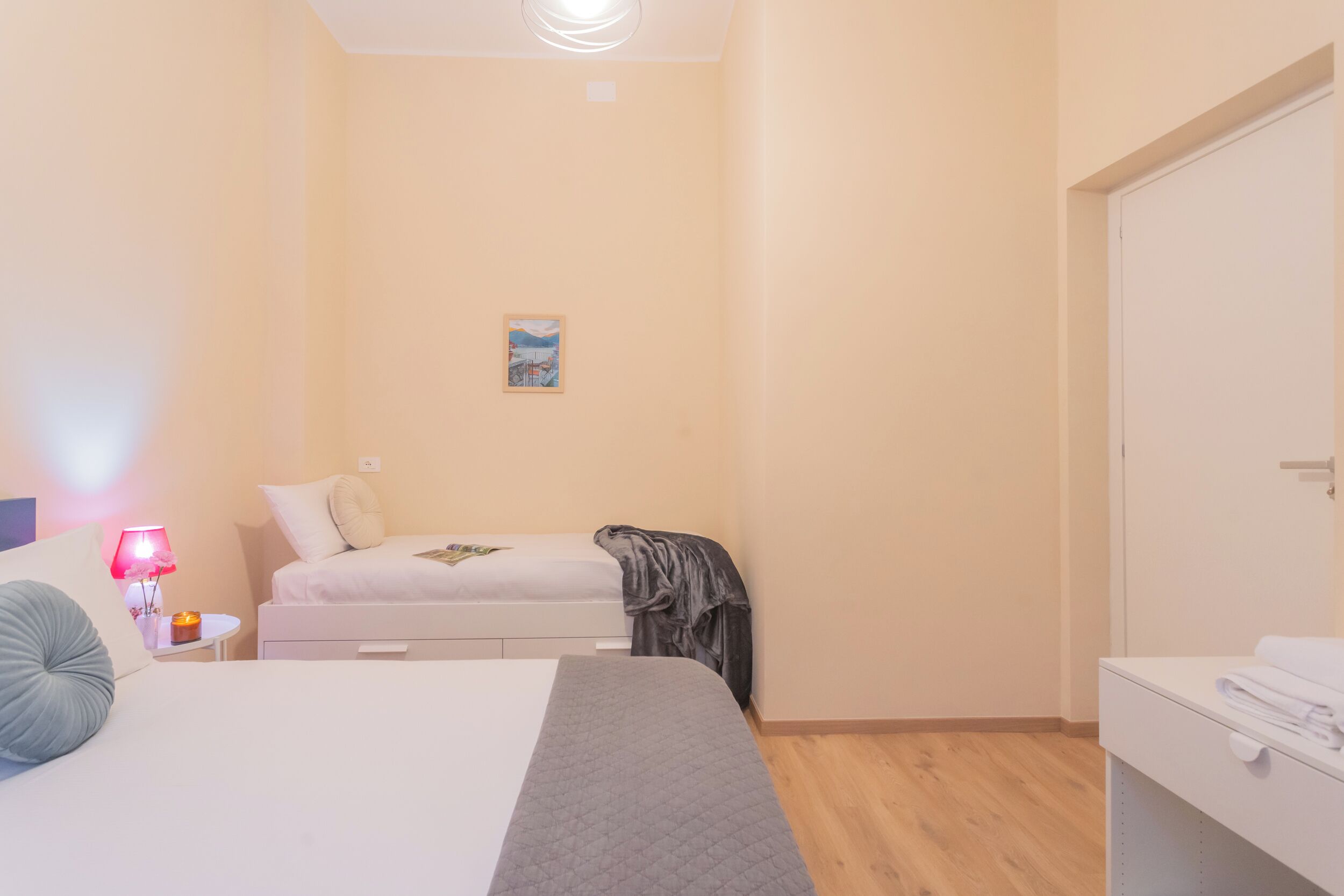 Un dormitorio con una cama, una mesita de noche con lámpara, un cuadro pequeño en la pared y un armario.