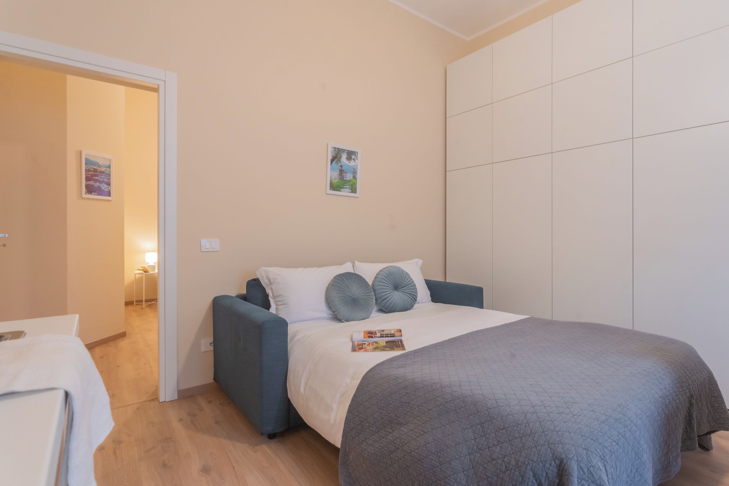 Een slaapkamer met een bed, een blauwe fauteuil, een witte kledingkast en een deur naar een andere kamer.