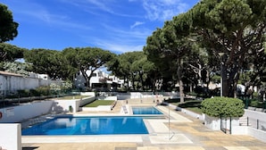 A pool area with two pools, surrounded by trees and a white building in the background. - Albufeira Açoteias Villa by Homing (Albufeira)